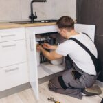 Professional,Plumber,Wearing,Safety,Glasses,Working,Under,Kitchen,Sink,Using