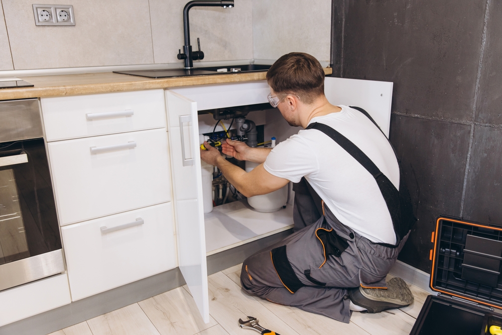 Professional,Plumber,Wearing,Safety,Glasses,Working,Under,Kitchen,Sink,Using